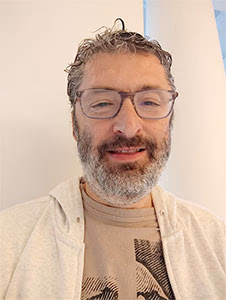 Hombre con barba y gafas sonriendo frente a una pared blanca