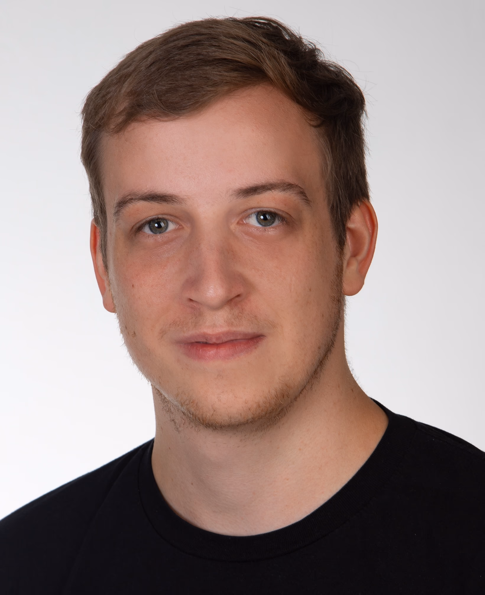 Porträt eines jungen Mannes mit kurzen Haaren und Bart, der ein schwarzes T-Shirt trägt.