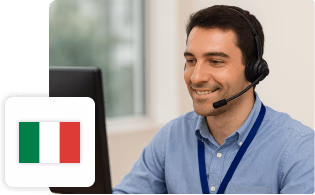 Operatore del servizio clienti con cuffie e microfono davanti al computer, affiancato dalla bandiera italiana.