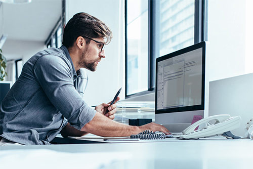 Un homme qui travaille sur un ordinateur et tient un stylo à la main