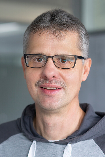 Mann mit Brille und Schnurrbart lächelt in die Kamera.