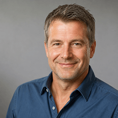 Mann mit kurzen Haaren und blauem Hemd lächelt in die Kamera.